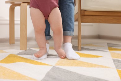 Mother supporting her baby son while he learning to walk on carpet at home, closeup