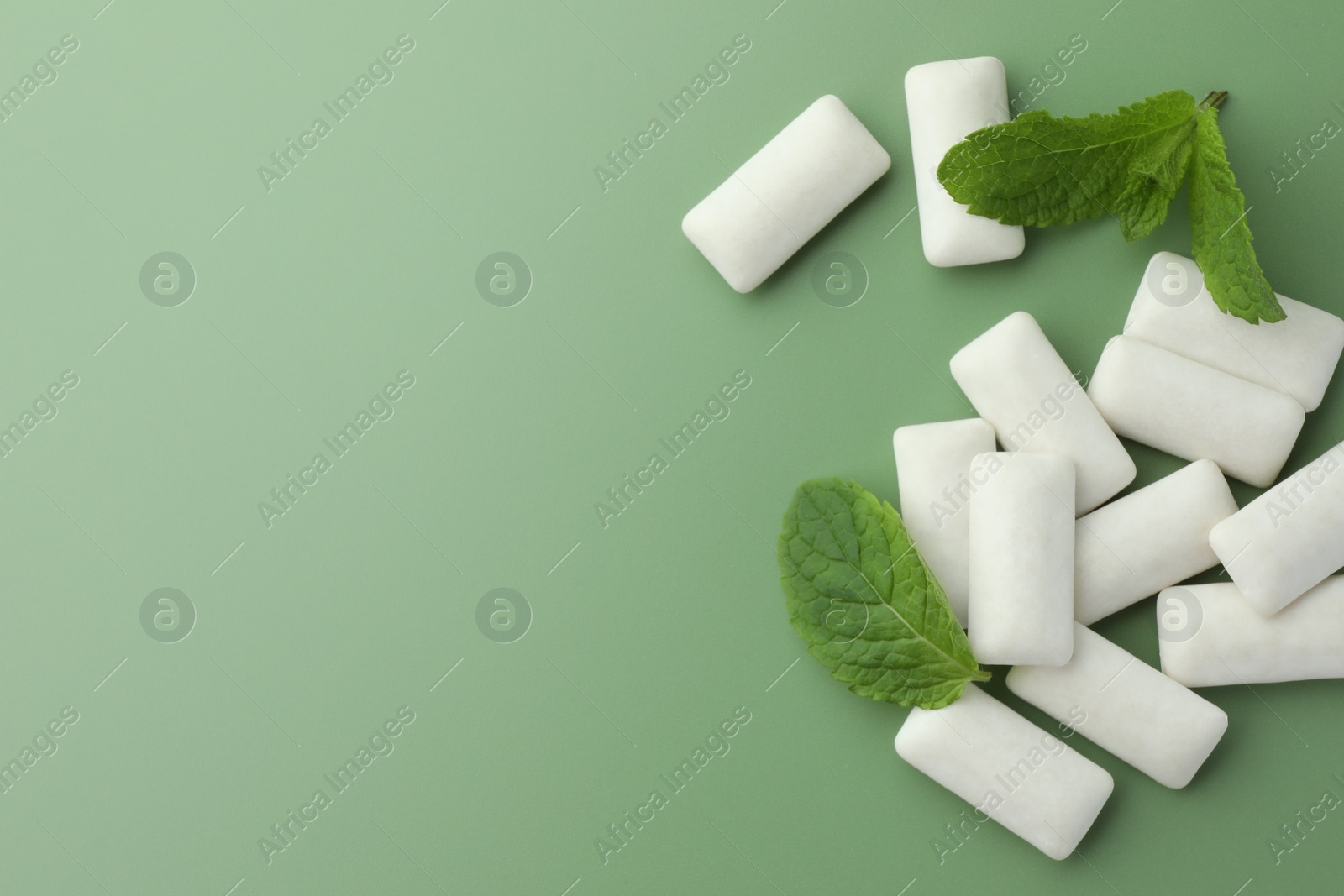 Photo of Tasty white chewing gums and mint leaves on light green background, flat lay. Space for text