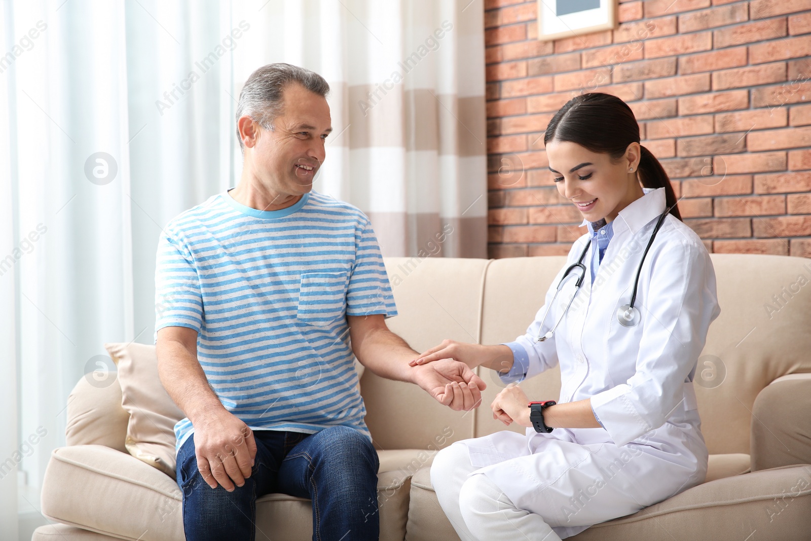 Photo of Doctor checking mature man's pulse with fingers at home