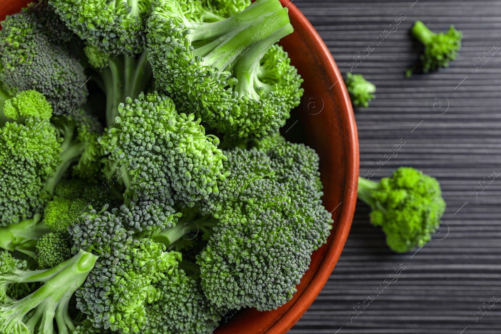 Photo of Bowl with fresh raw broccoli on black wooden table, flat lay