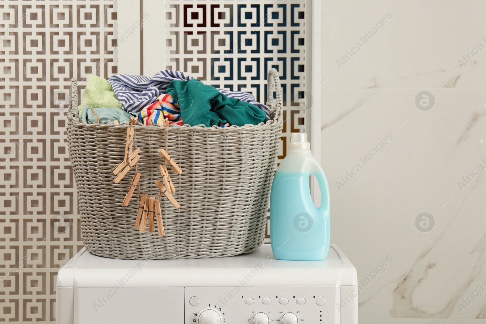 Photo of Wicker basket with dirty clothes and detergent bottle on washing machine in laundry room