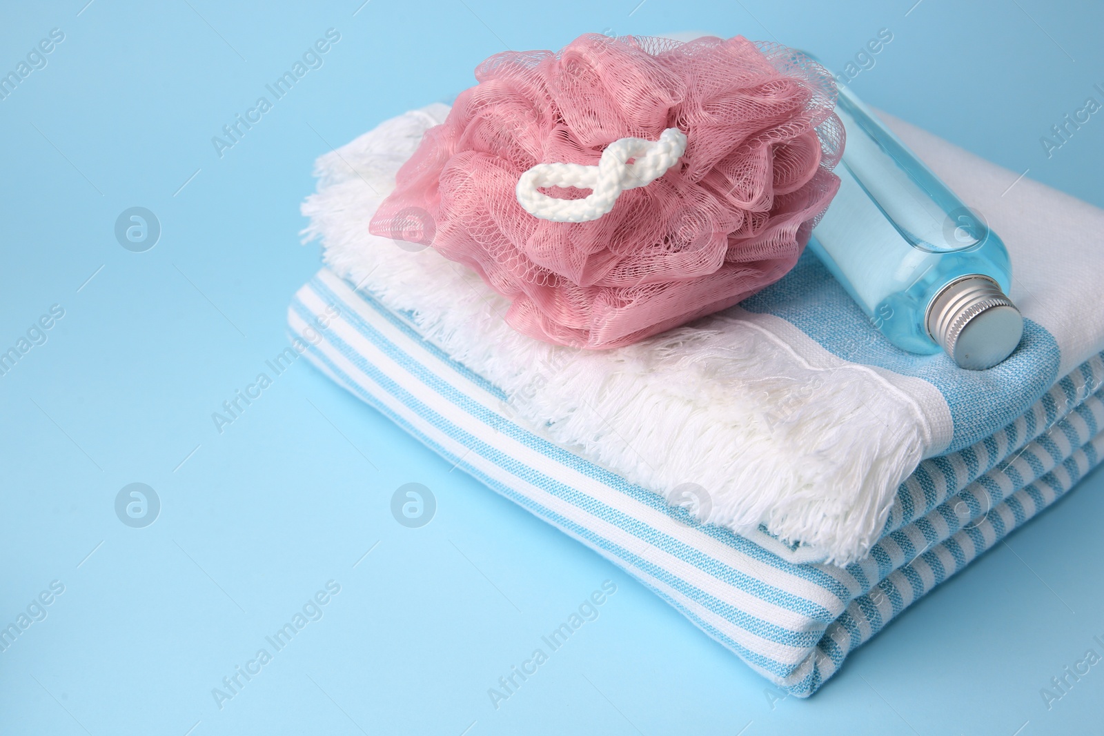 Photo of Pink shower puff, bottle of cosmetic product and towel on light blue background, space for text