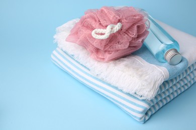 Pink shower puff, bottle of cosmetic product and towel on light blue background, space for text