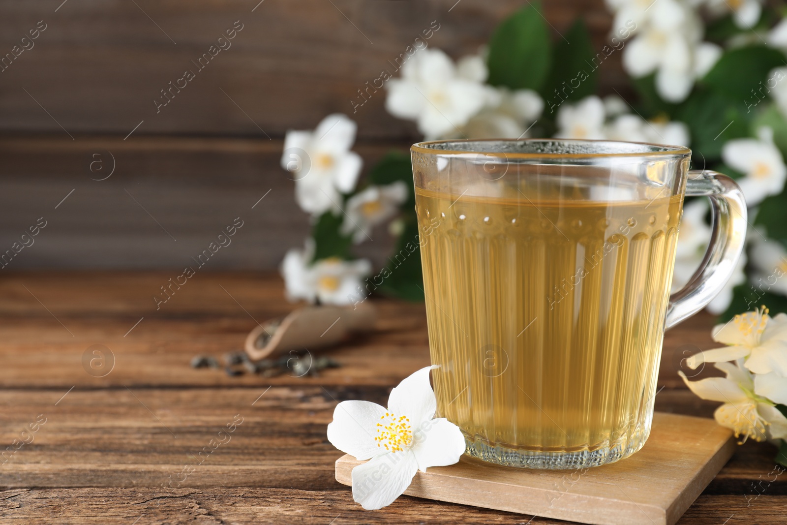 Photo of Cup of tea and fresh jasmine flowers on wooden table. Space for text