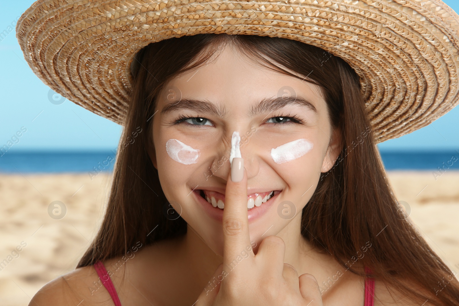 Image of Teenage girl with sun protection cream on her face near sea, closeup