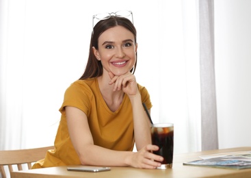 Photo of Young woman with glass of cola at table indoors. Refreshing drink