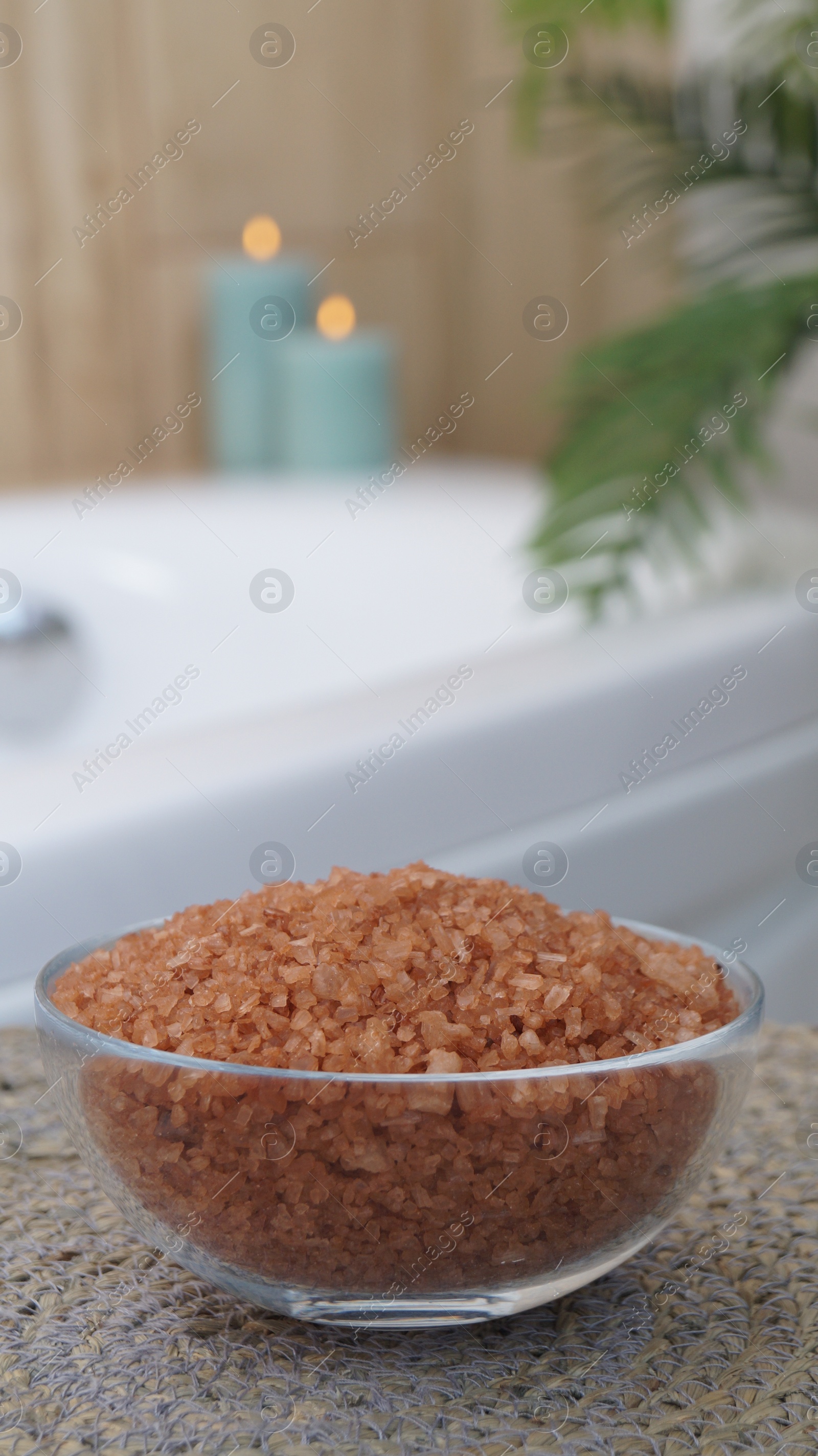 Photo of Glass bowl of bath salt on wicker mat in bathroom