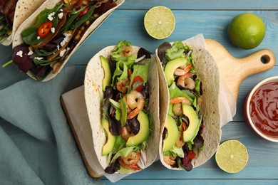 Photo of Delicious tacos with shrimps, avocado and lime on turquoise wooden table, flat lay