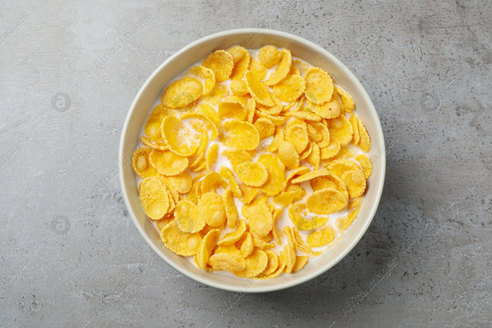 Photo of Tasty crispy corn flakes with milk on light grey table, top view