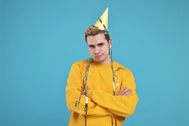 Sad young man with party hat on light blue background