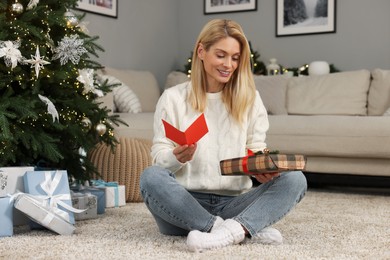 Photo of Happy woman with Christmas gift and greeting card at home