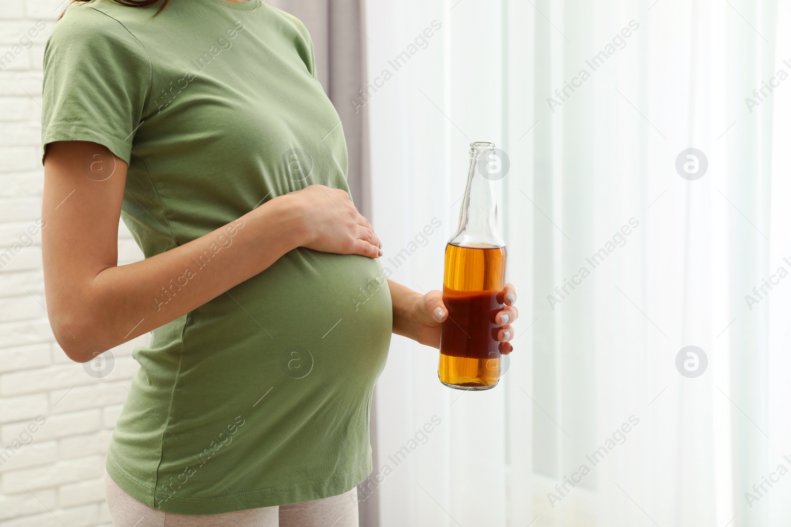 Photo of Pregnant woman with bottle of beer indoors, closeup. Alcohol abuse during pregnancy