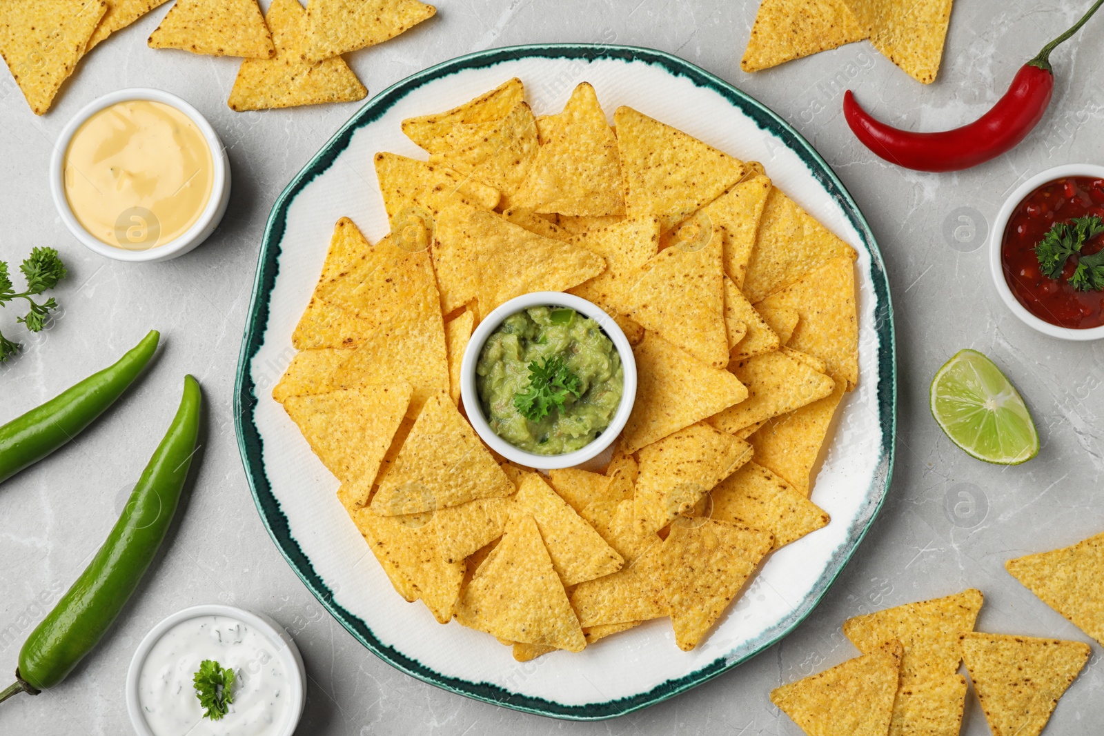 Photo of Mexican nacho chips with different sauces on grey marble background, flat lay