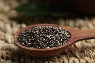 Photo of Wooden spoon with chia seeds on wicker stand, closeup