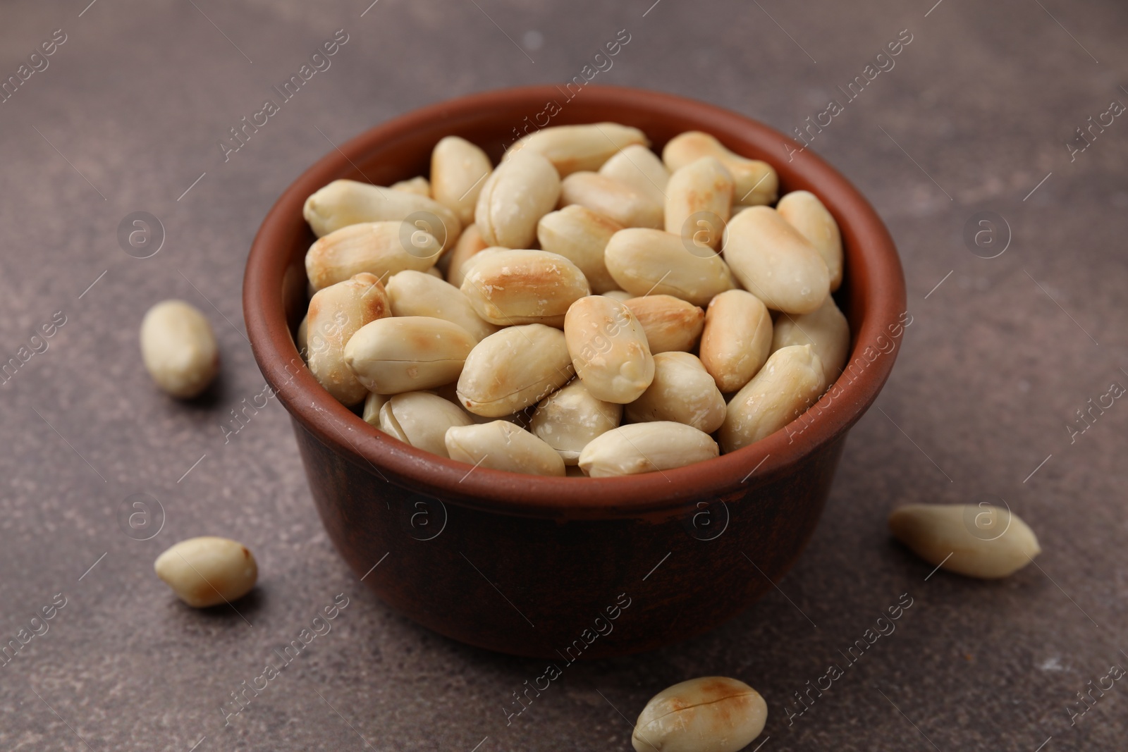 Photo of Roasted peanuts in bowl on brown table, closeup