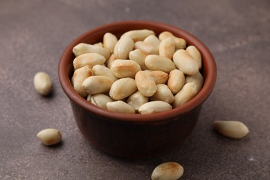 Roasted peanuts in bowl on brown table, closeup