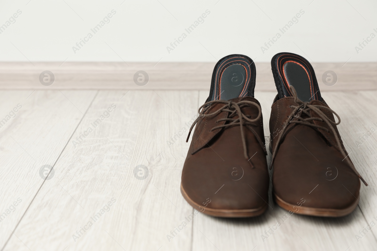 Photo of Orthopedic insoles in shoes on floor, closeup. Space for text