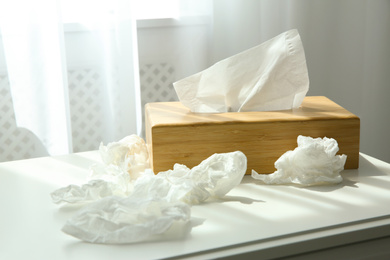 Photo of Used paper tissues and wooden holder on table near window