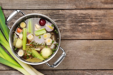 Photo of Different ingredients for cooking tasty bouillon in pot and celery on wooden table, flat lay. Space for text