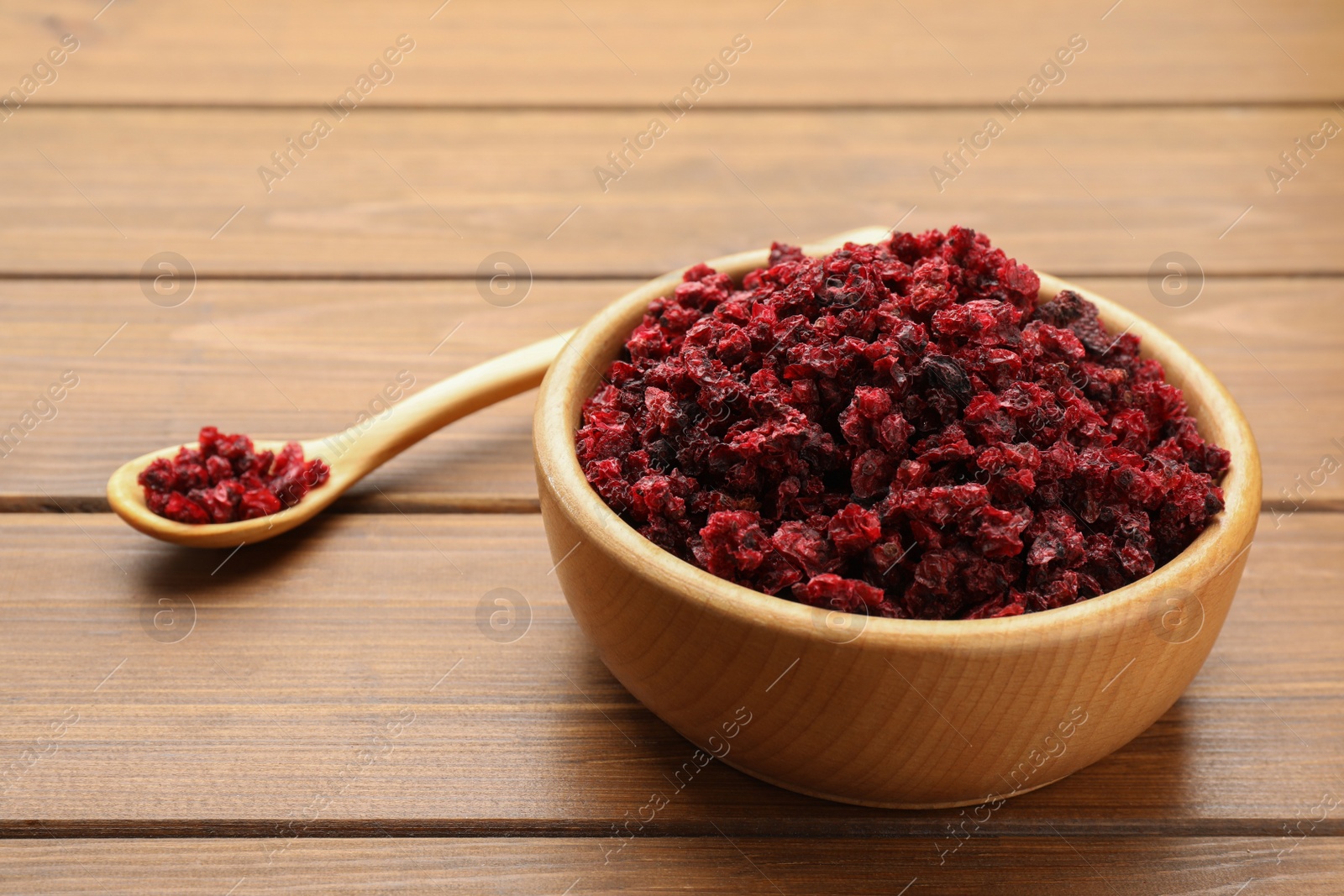 Photo of Dried red currants in bowl and spoon on wooden table