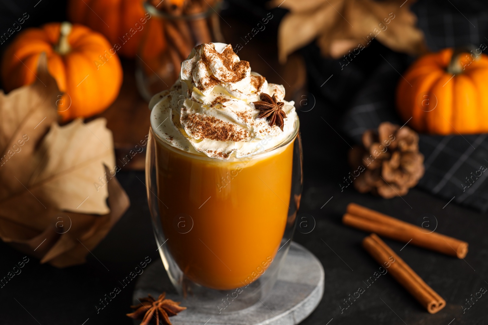 Photo of Glass of pumpkin spice latte with whipped cream and ingredients on black table, closeup