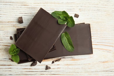 Tasty dark chocolate pieces with mint on white wooden table, flat lay