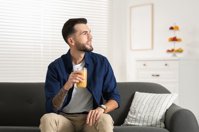 Photo of Handsome man with delicious smoothie on sofa at home. Space for text