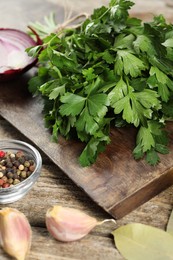 Board with fresh parsley, peppercorns and other products on wooden table, closeup