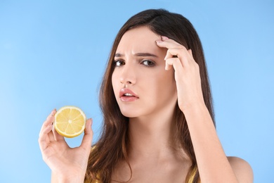 Teenage girl with acne problem holding lemon against color background