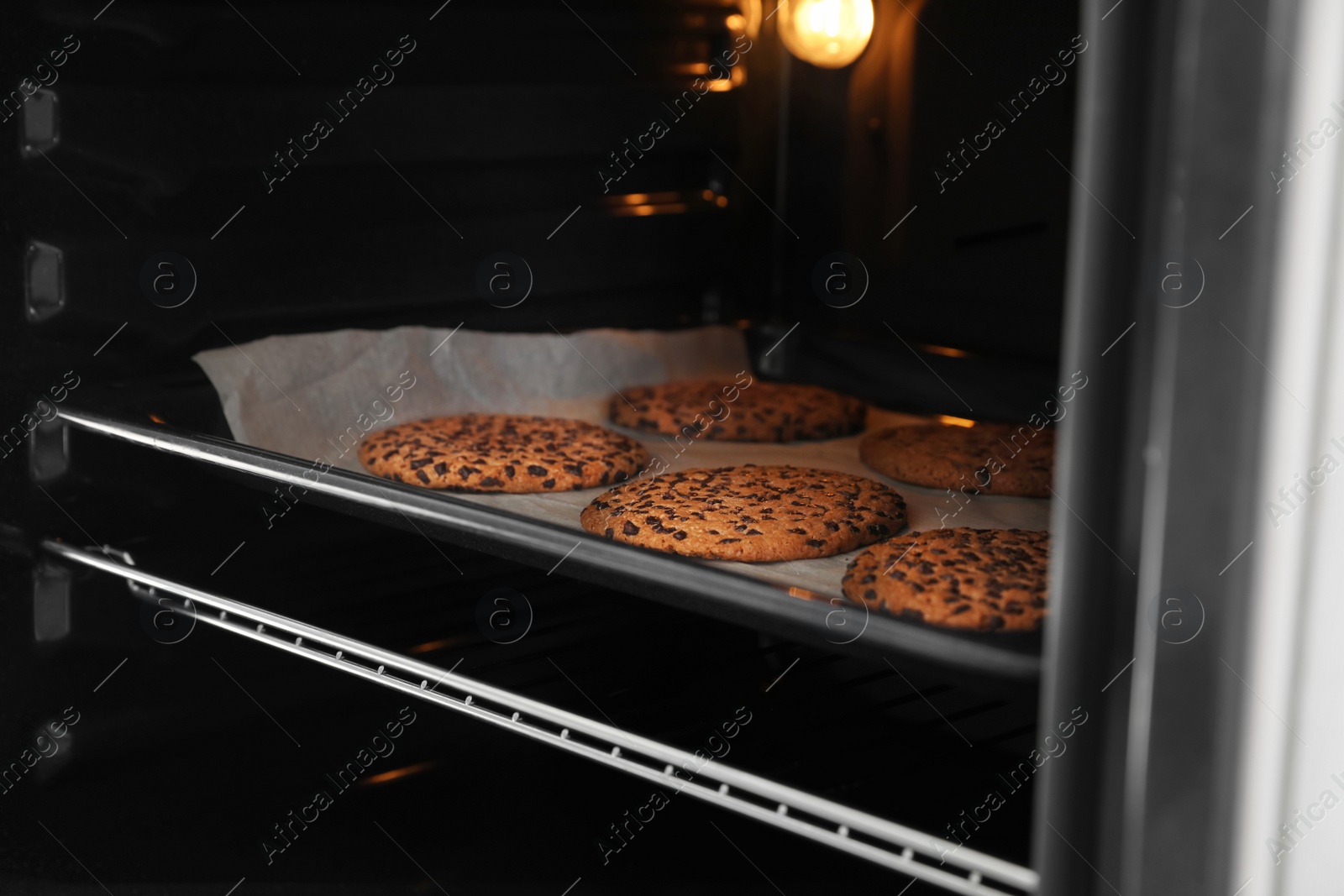 Photo of Open modern oven with freshly baked cookies on sheet, closeup