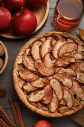 Photo of Delicious apple pie, ingredients and cup of tea on wooden table, flat lay