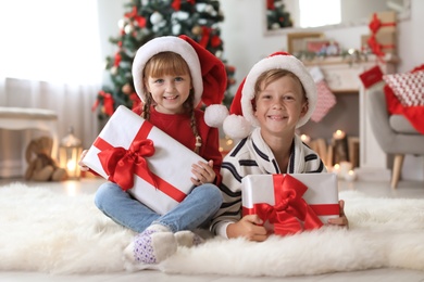 Photo of Cute little children in Santa hats with Christmas gift boxes at home