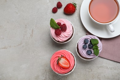 Different delicious cupcakes with cream and berries on light grey table, flat lay. Space for text