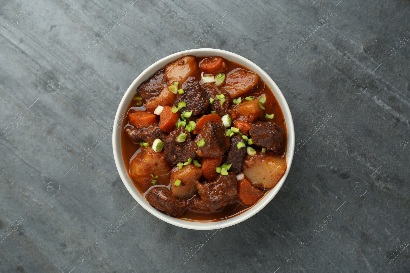 Photo of Delicious beef stew with carrots, green onions and potatoes on grey table, top view