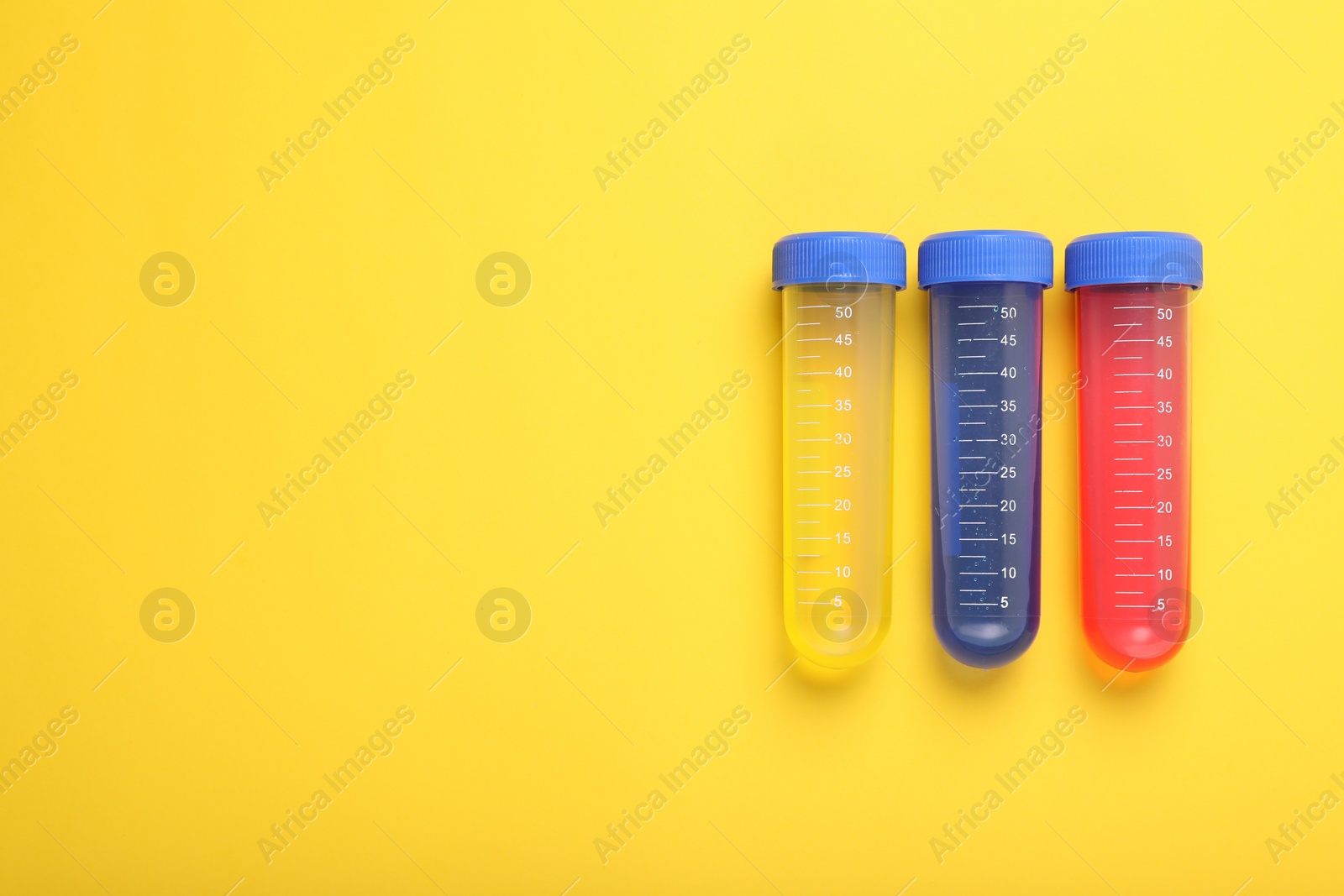 Photo of Test tubes with colorful liquids on yellow background, flat lay and space for text. Kids chemical experiment set