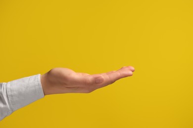 Woman holding something in hand on yellow background, closeup. Space for text