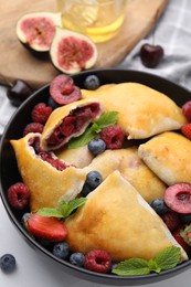 Photo of Bowl with delicious samosas, berries and mint leaves on white tiled table, closeup