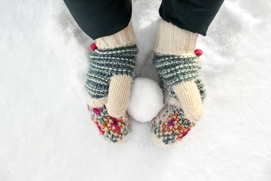 Photo of Woman in knitted mittens making snowball outdoors, top view