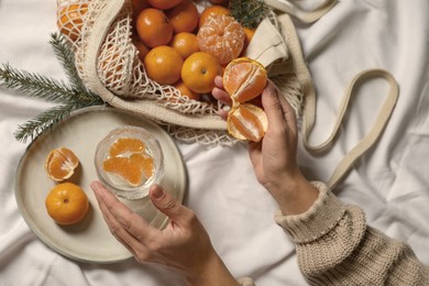 Woman with delicious ripe tangerines and glass of sparkling wine on white bedsheet, top view