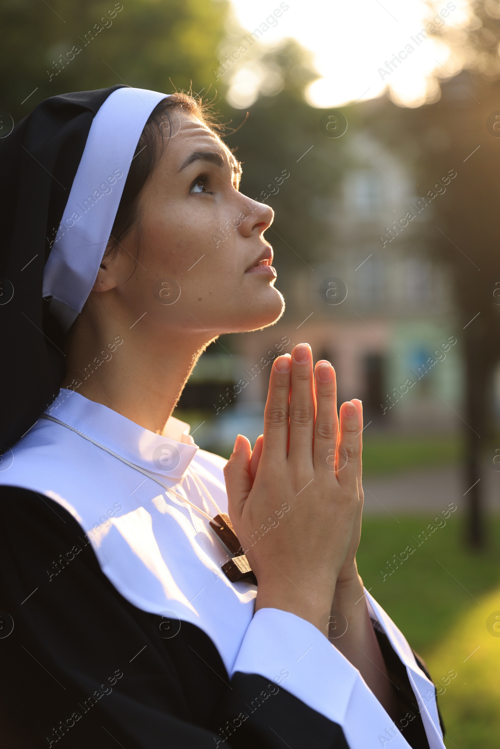 Photo of Young nun with hands clasped together praying outdoors on sunny day