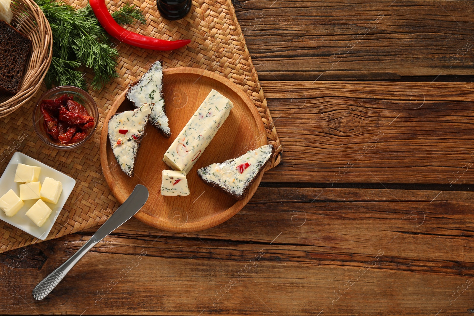 Photo of Tasty butter, dill, chili peppers and rye bread on wooden table, top view. Space for text