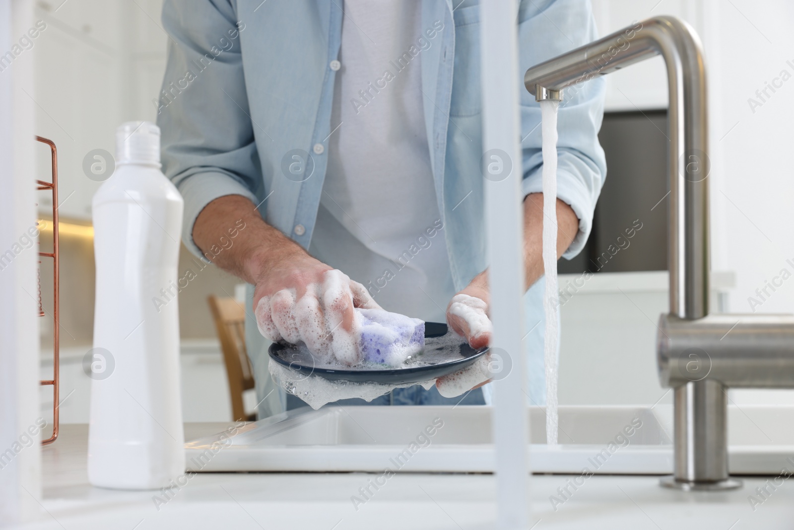 Photo of Man washing plate above sink in kitchen, closeup