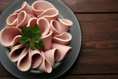 Photo of Slices of delicious boiled sausage with parsley on wooden table, top view. Space for text