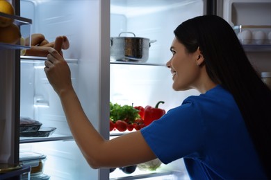 Young woman taking sausages out of refrigerator at night