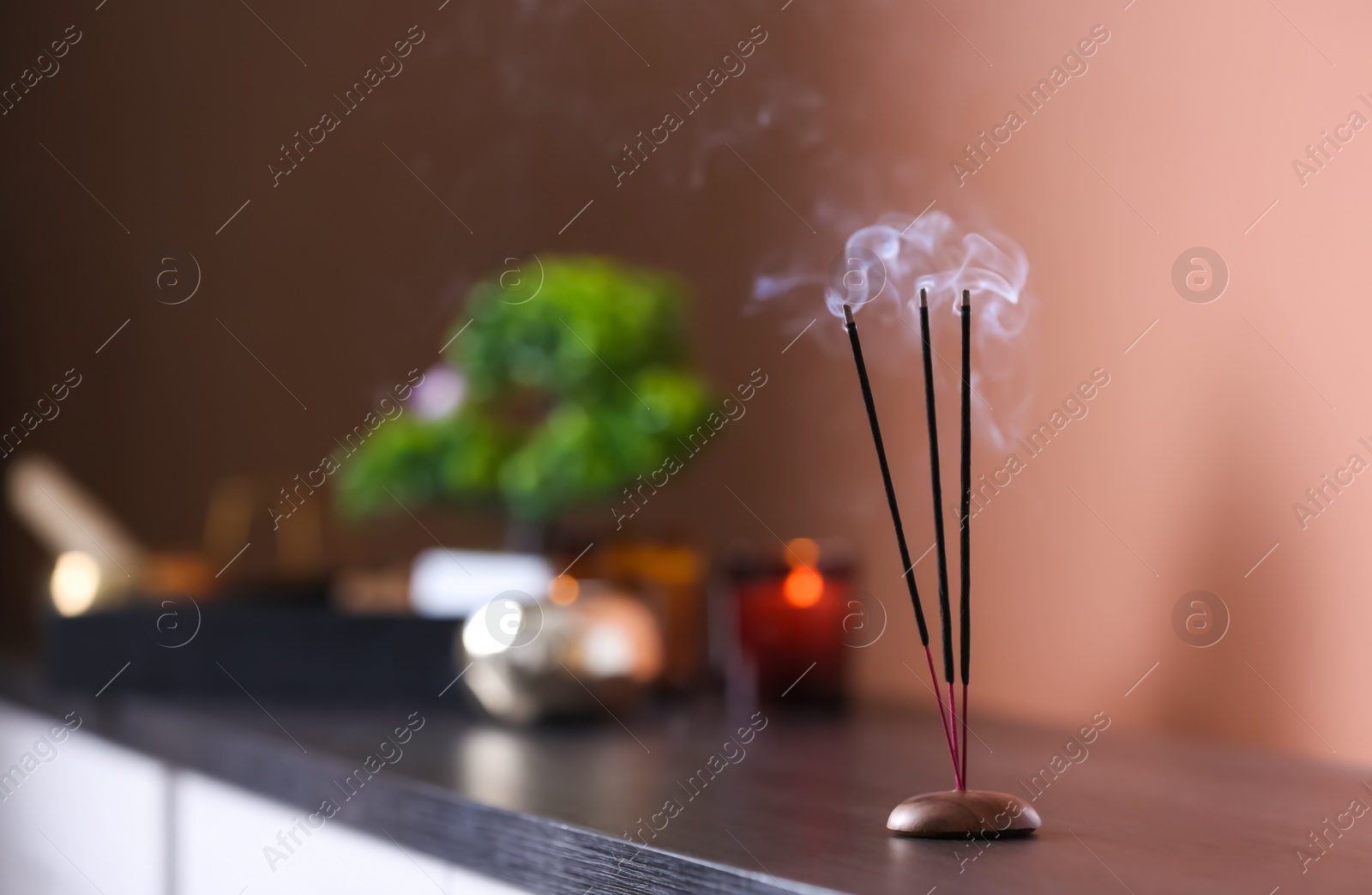 Photo of Incense sticks smoldering on wooden table in room. Space for text