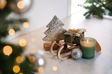 Photo of Toy sleigh with gift box, decorative Christmas tree, candle and ball on white countertop indoors