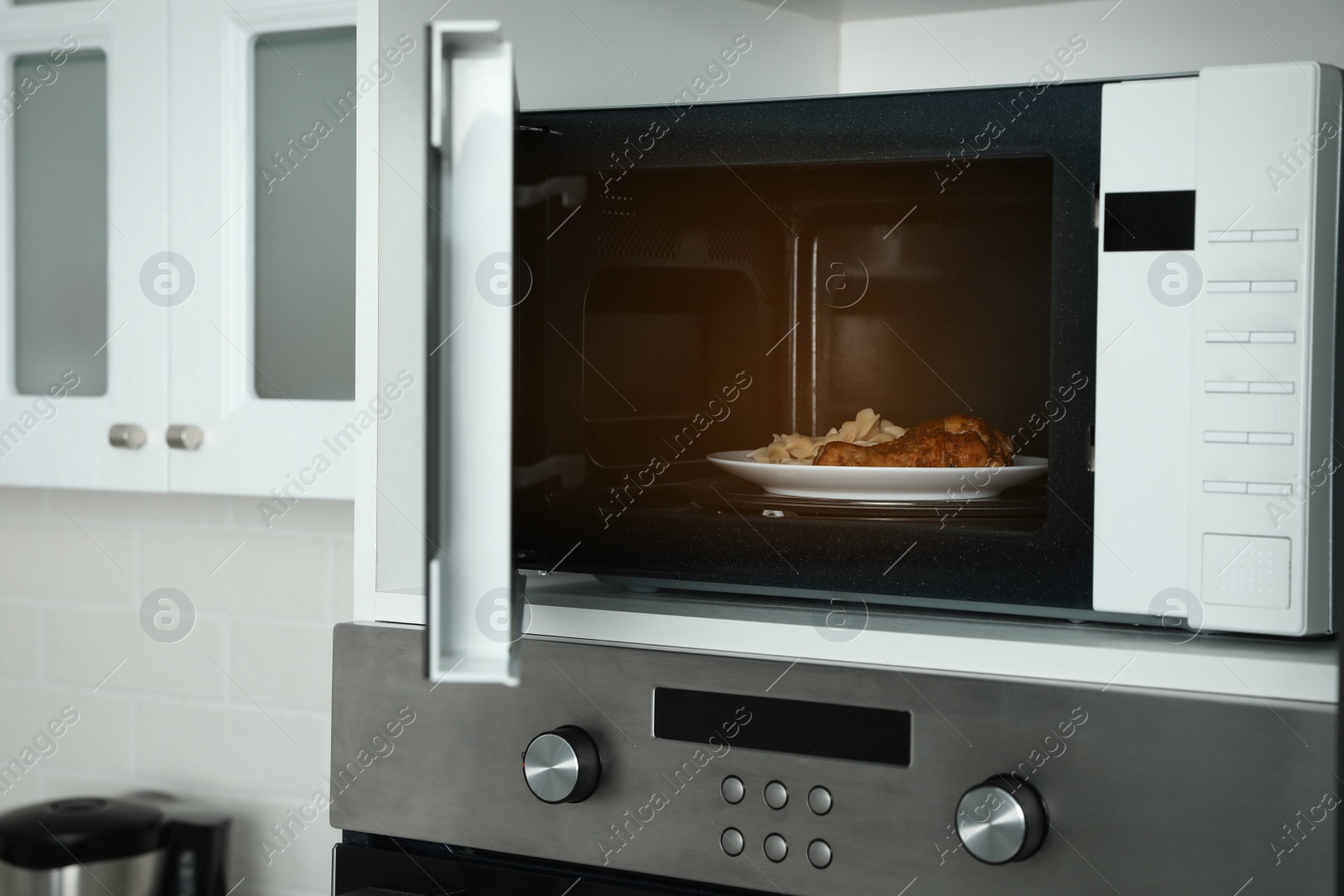 Photo of Open microwave oven with food on white shelf in kitchen