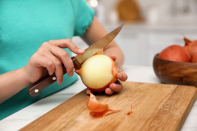 Photo of Little girl peeling onion at table in kitchen, closeup. Preparing vegetable