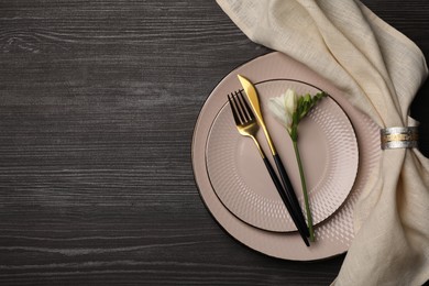 Stylish table setting. Plates, cutlery, napkin and floral decor on dark wooden background, top view with space for text