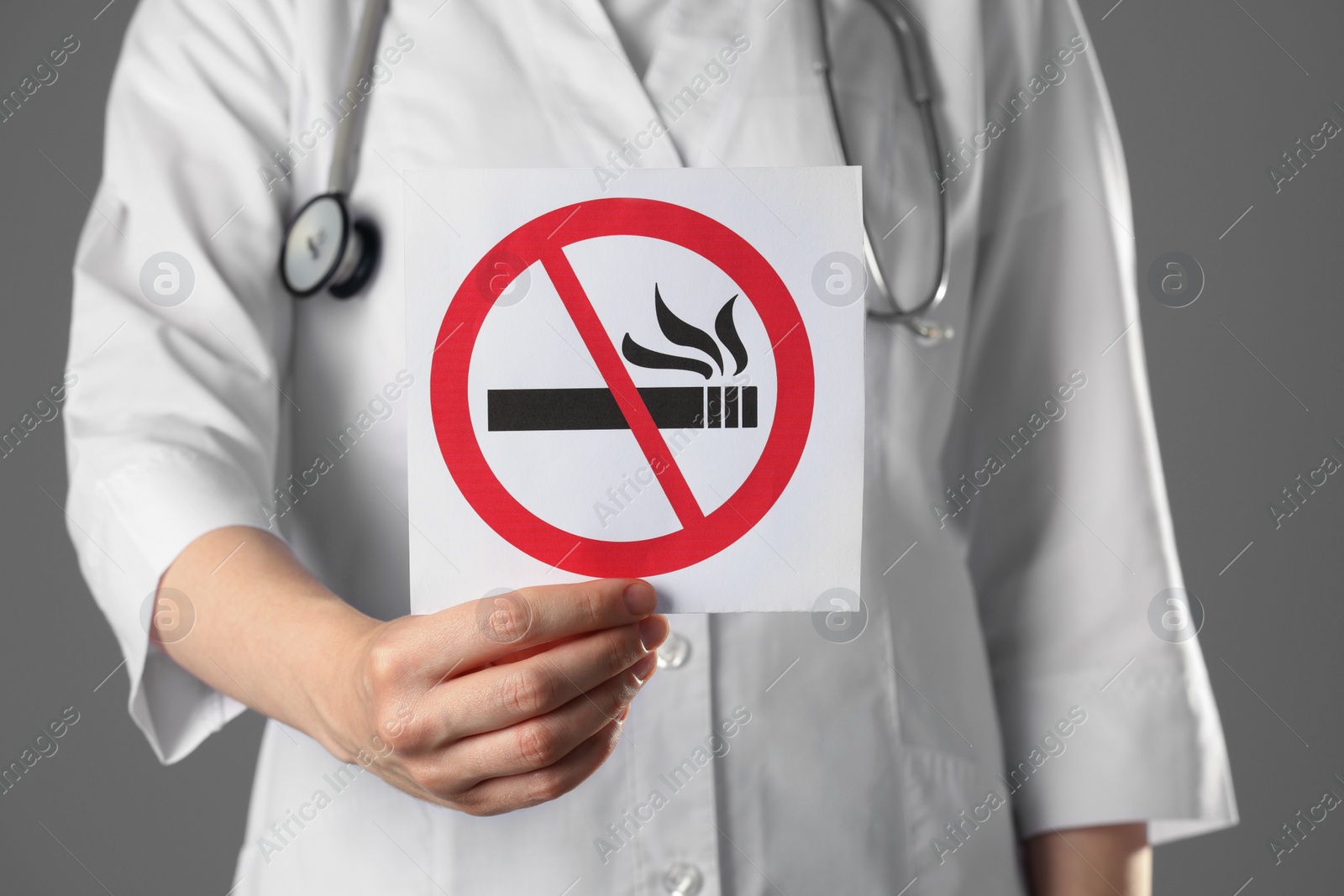 Photo of Doctor holding card with no smoking sign on gray background, closeup